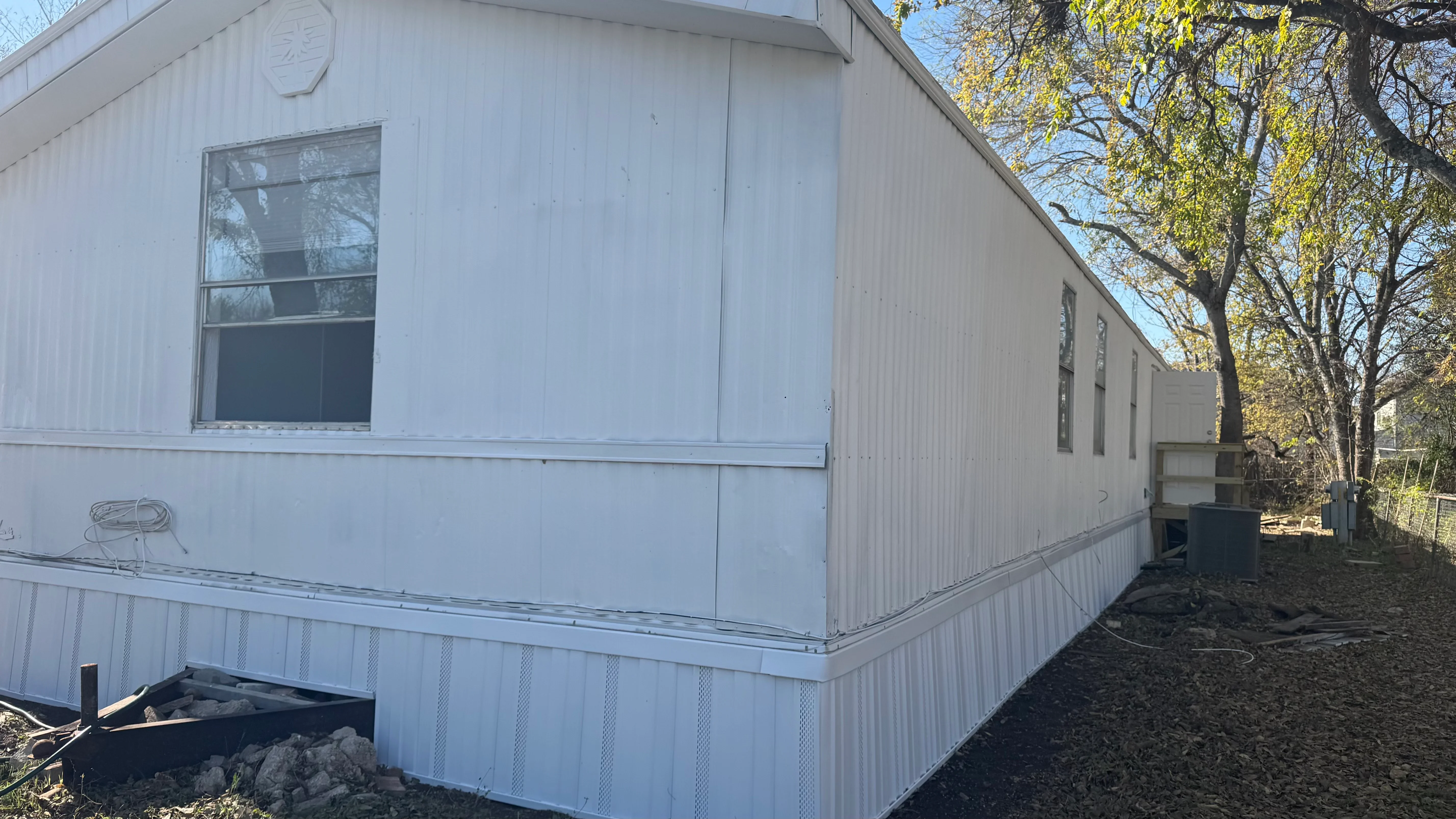 White corrugated metal siding with trim, windows, and mesh foundation skirting on mobile home