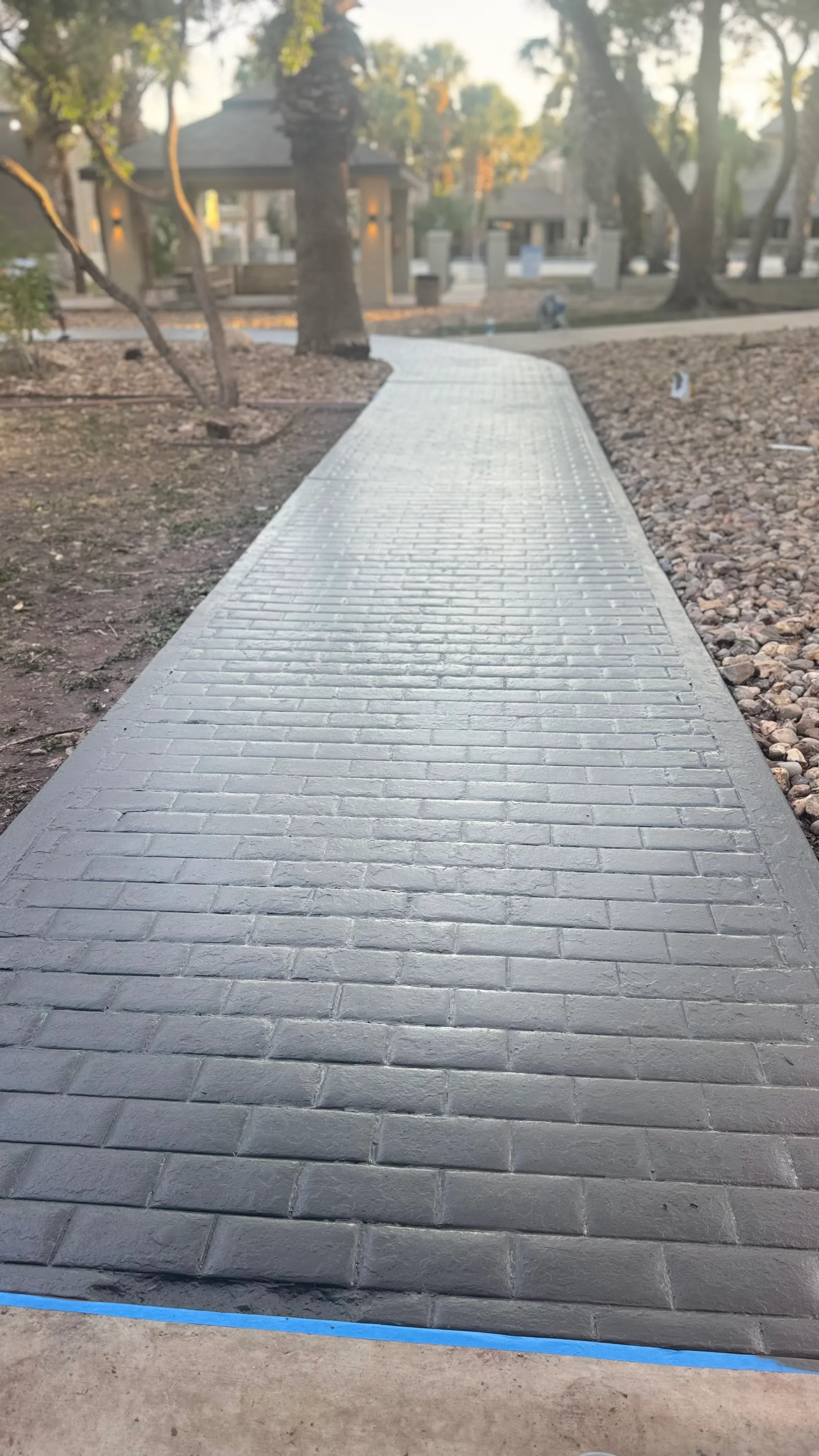 Gray concrete permeable pavers in running bond pattern forming a straight walkway through landscaped grounds with trees