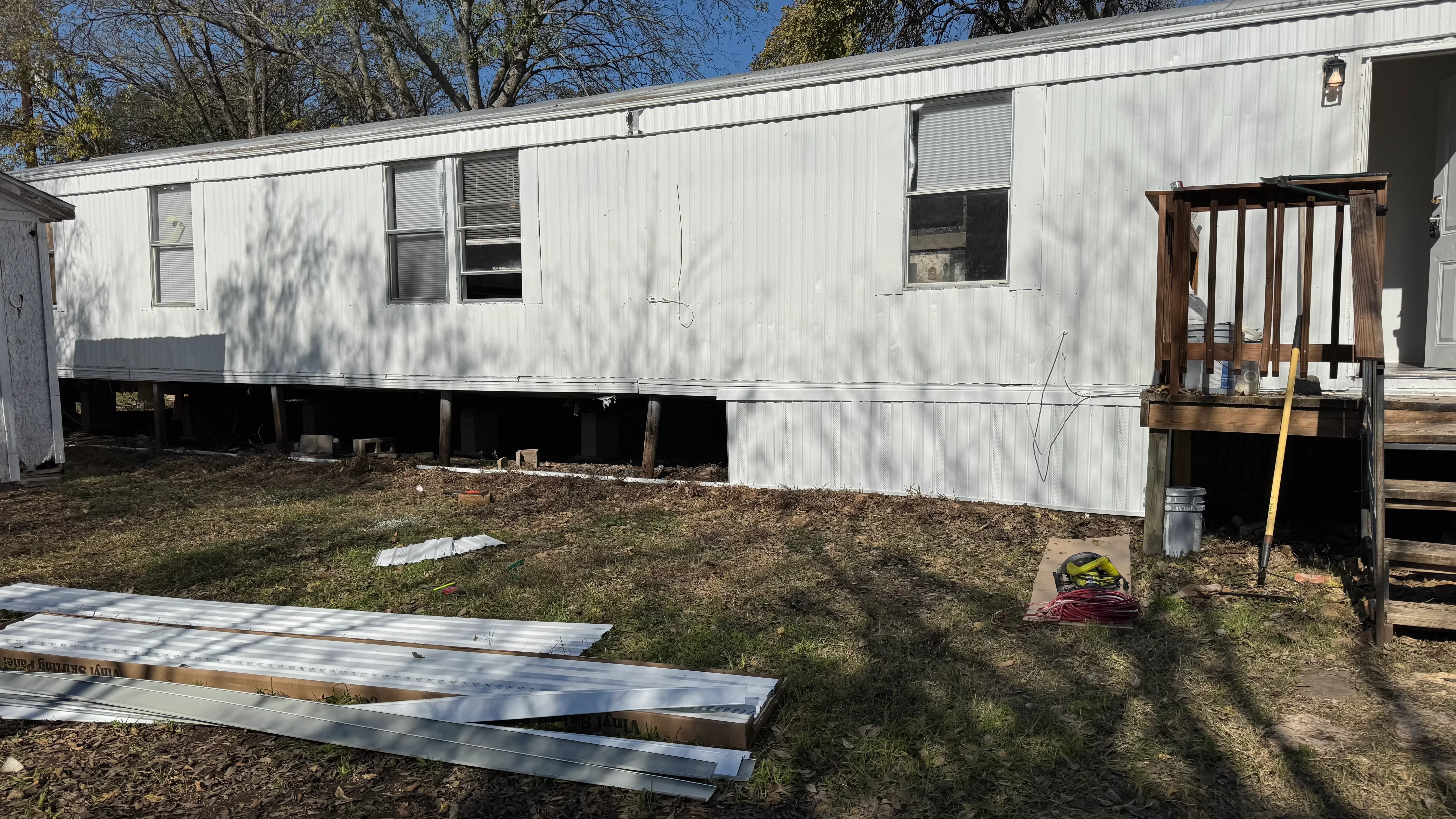 Mobile home with metal siding, staged roofing materials, and wooden deck frame